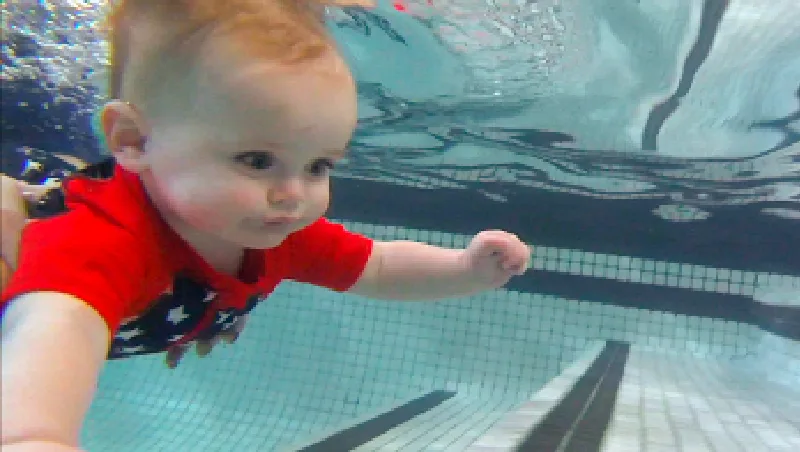 A baby swimming underwater toward the pool steps
