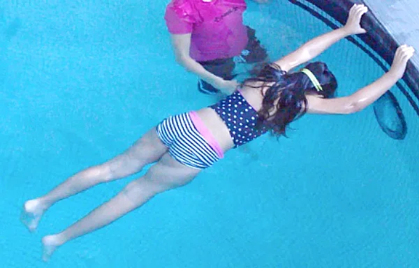 A child practicing a front float in the deep end